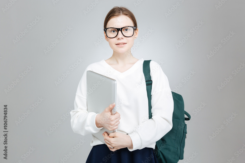 Smiling teenage girl in glasses holding green backpack and laptop Smiling teenage girl in glasses holding green backpack and laptop