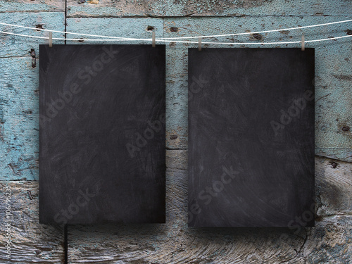 Close-up of two blank blackboard frames hanged by pegs against blue and brown wooden background