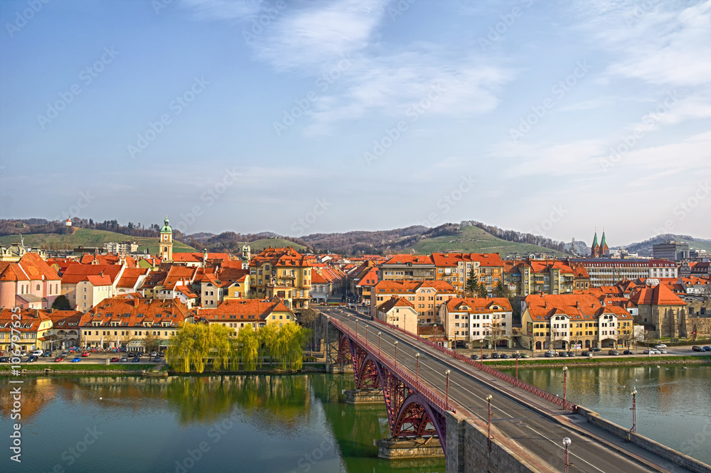 Maribor, Slovenia, Europe. Main bridge (Glavni most, Stari most) over the Drava river. Popular riverbank Lent in  the background.