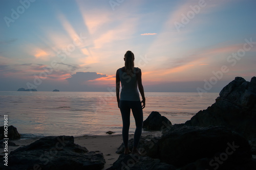 The girl at sunset standing on the seashore, the colourful sky 