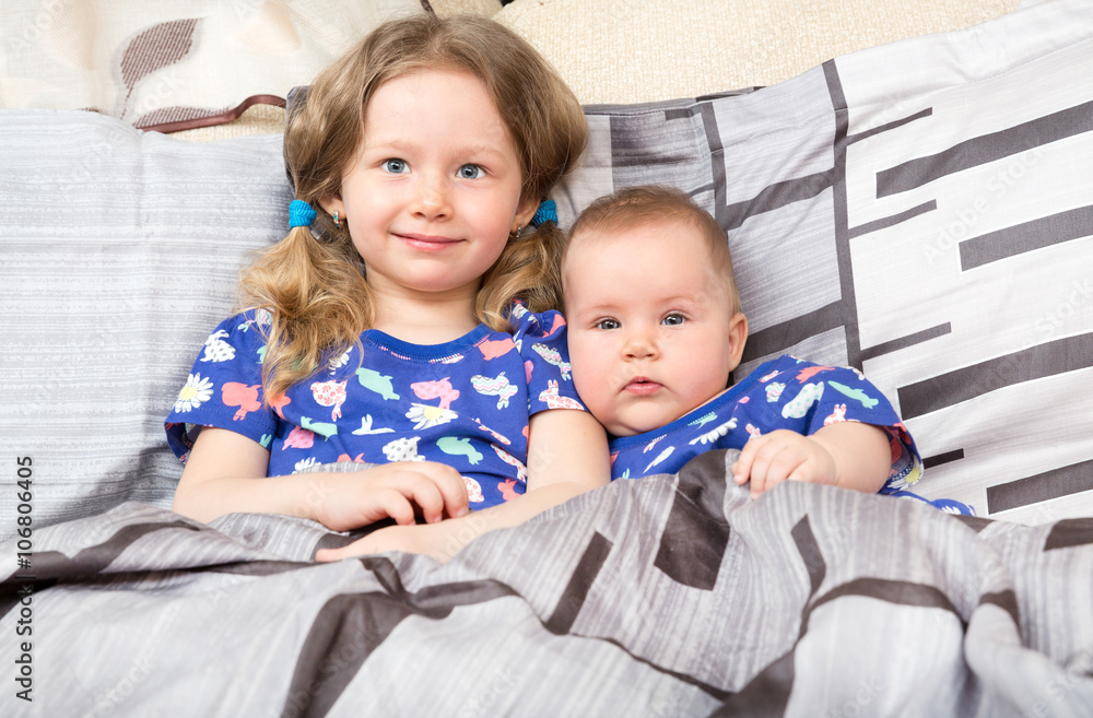 Two sisters. Older sister kid hugging his newborn little sister. Cute children girls on bed at home. Two sisters. Older sister kid hugging his newborn little sister. Cute children girls on bed at home.