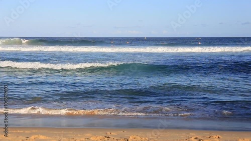 Big beautiful blue waves break with spray on the sandy beach and the surfers ride the huge waves in the Australian beach in fine clear weather