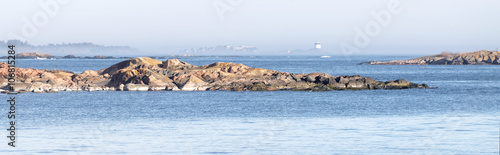 Coast, cliffs and a distant beacon surrounded with fog sunny day