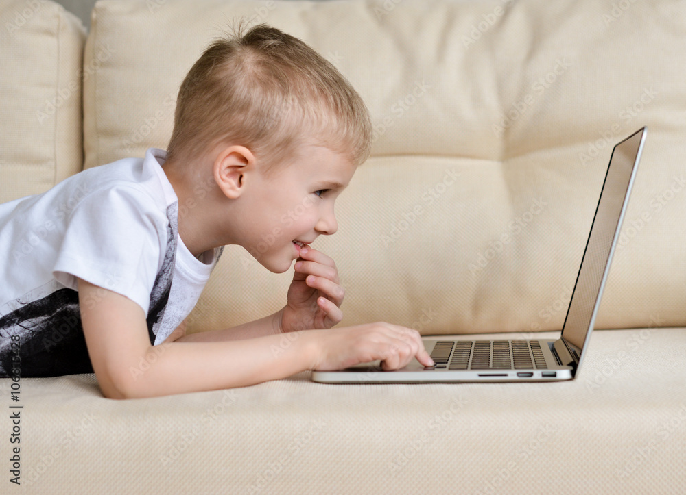 Portrait a little boy stretched out on sofa in front of laptop computer Portrait a little boy stretched out on sofa in front of laptop computer