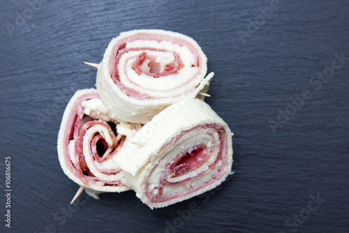 Rolls of flat bread with salami on slate top seen from above
