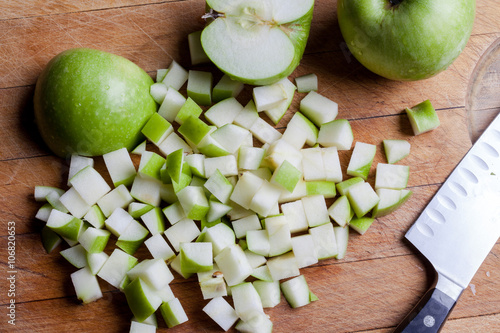 Cut granny smith green apples on wooden cutting board with knife from above