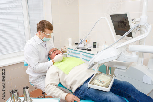 Young dentist without assistant treating elderly man