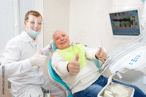 Young doctor dentist and old senior man patient showing thumb up, smiling and happy looking at the camera