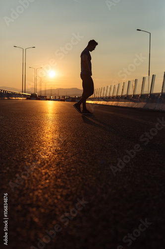 Attractive fit man running fast along big modern bridge at sunse