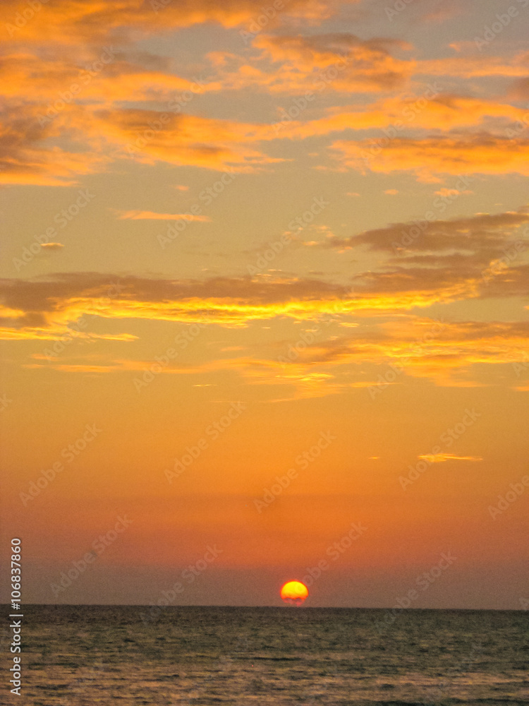 Spectacular sunset over the sea with red sun in a tropical landscape with colorful clouds on the horizon. Copy space.