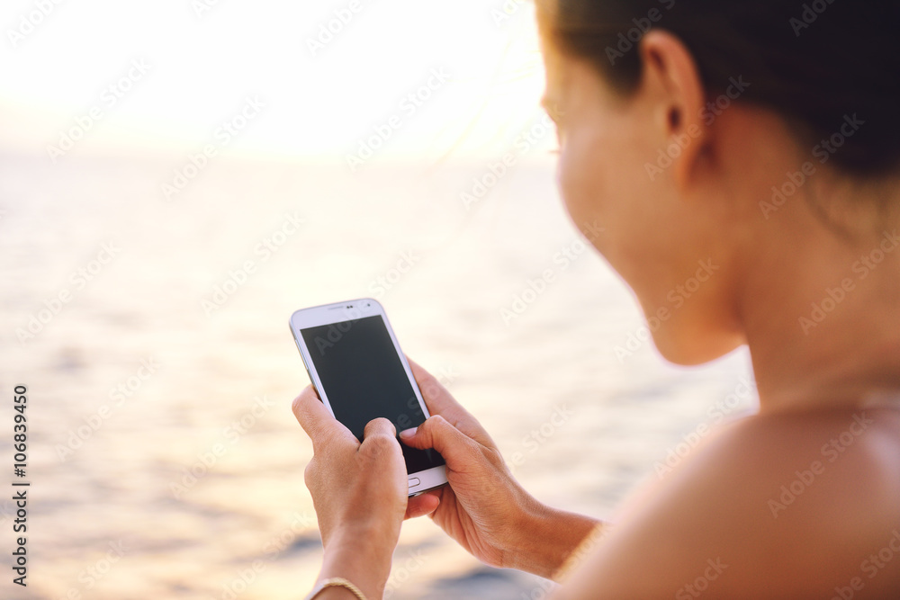 Smartphone woman texting on social media app looking at display screen for sms reading on ocean background on a sea cruise balcony or beach at sunset on holiday. Unrecognizable girl using smart phone.