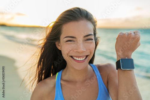 Smartwatch happy girl showing display screen on trendy new smart watch fitness tracker wristwatch. Healthy young Asian sporty woman smiling on beach vacation running at sunset living an active life.