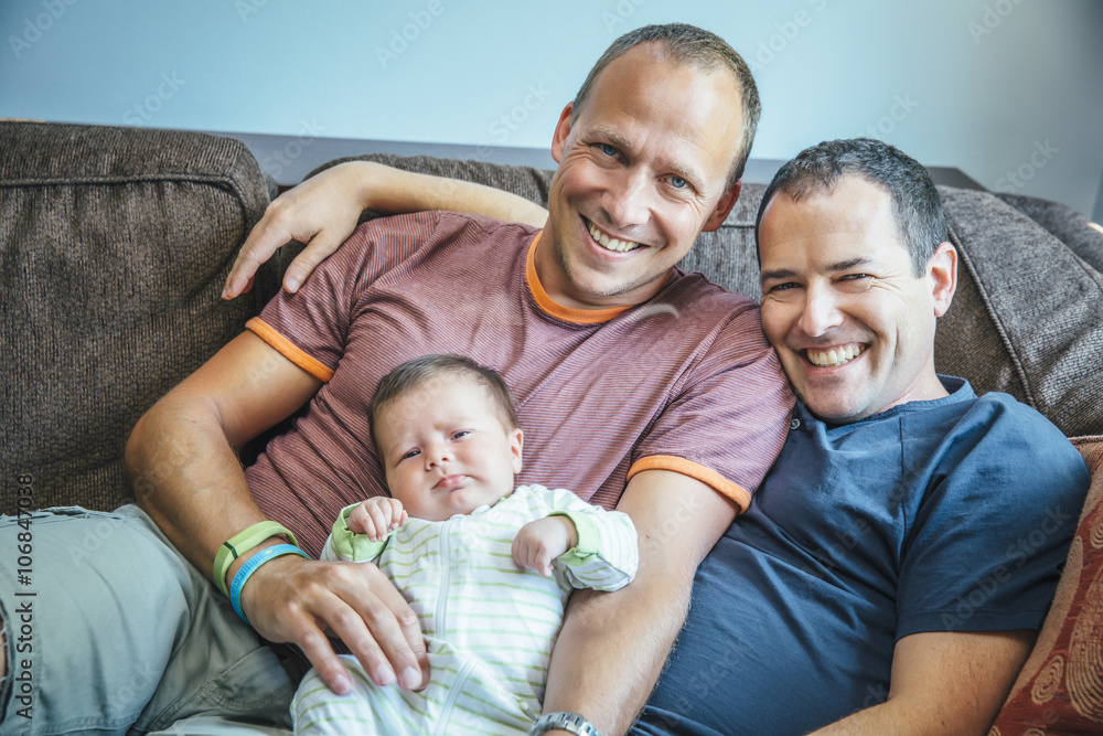 Caucasian gay couple smiling with baby boy on sofa Caucasian gay couple smiling with baby boy on sofa
