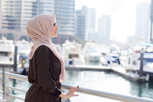 Smiling girl in hijab covering her eyes with happiness in Dubai Marina photo