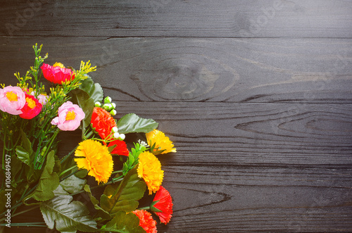 colorful Plastic flowers on black wooden table vintage tone