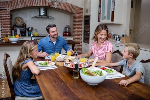 Quadro em tela Happy family talking to each other while having meal in kitchen