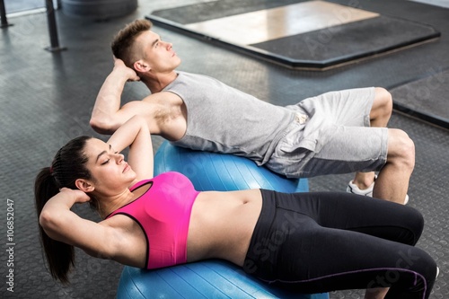 Fit couple doing abdominal crunches on fitness ball 