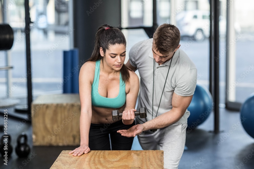 Fototapeta premium Male trainer assisting woman lifting dumbbells