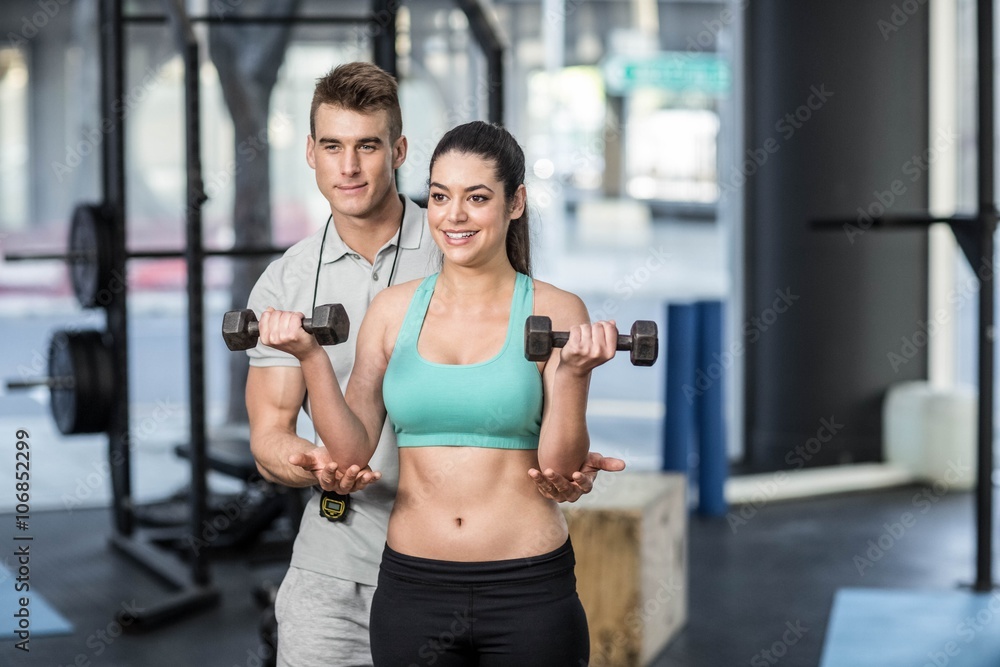 Male trainer assisting woman lifting dumbbells