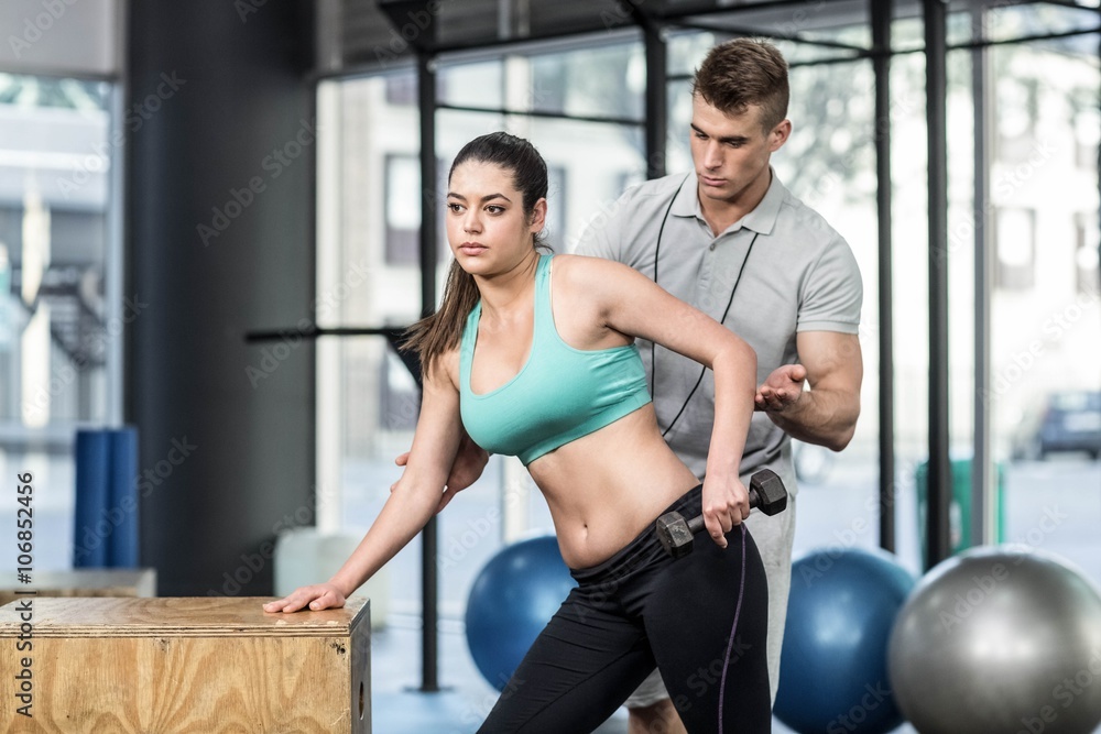 Naklejka premium Male trainer assisting woman lifting dumbbells