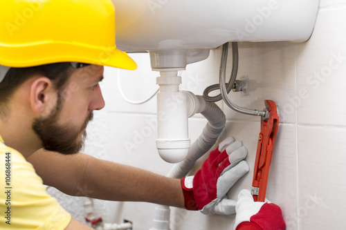 plumber fixing sink pipe with wrench in bathroom photo