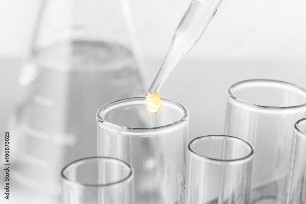 Laboratory pipette with drop of liquid over glass test tubes Laboratory pipette with drop of liquid over glass test tubes
