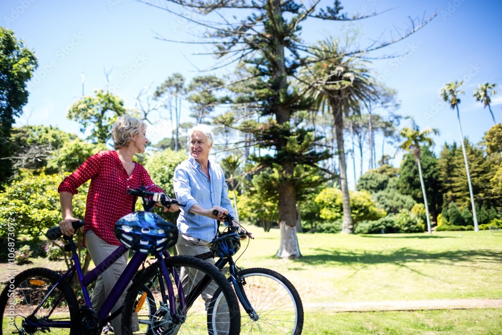 Senior couple walking with bicycle in park Senior couple walking with bicycle in park