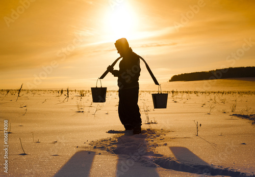 Silhouette of Mari man carrying buckets on traditional yoke in snowy field