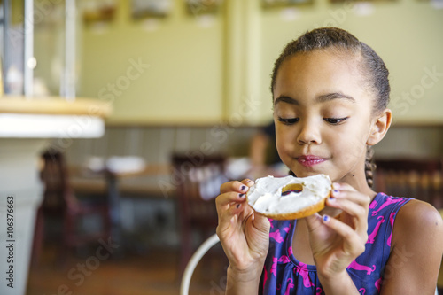 Mixed race girl eating bagel in cafe