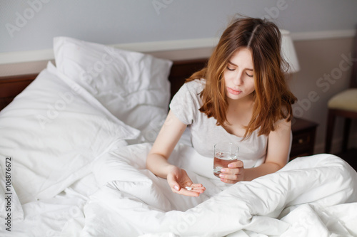 Sick woman looking on pills in her hand