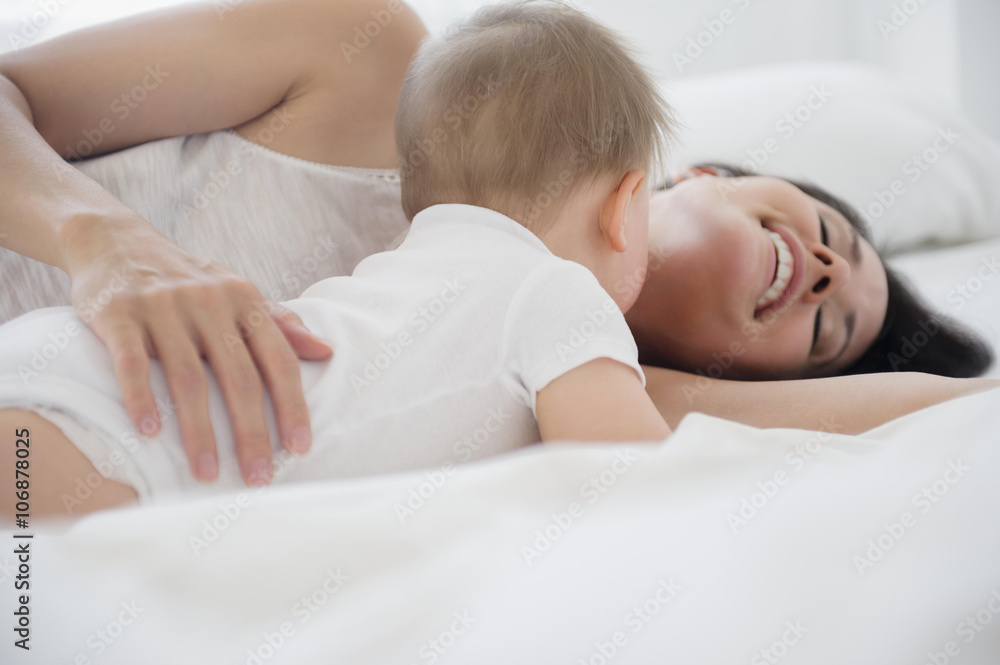 Mixed race mother playing with baby on bed Mixed race mother playing with baby on bed