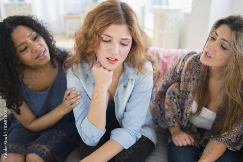 Women comforting sad friend on sofa in living room photo