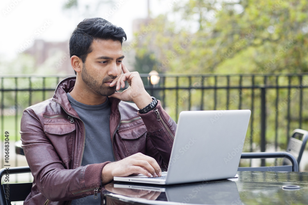 Indian man using laptop at table outdoors Indian man using laptop at table outdoors