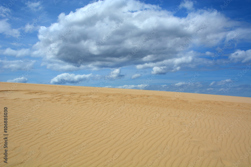 Sand dune with blue sky and puffy clouds