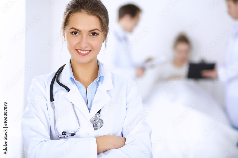 Female doctor smiling on the background with patient in the bed and two doctors Female doctor smiling on the background with patient in the bed and two doctors