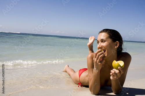 Quadro em tela femme qui mange une orange allongée sur le sable à la mer