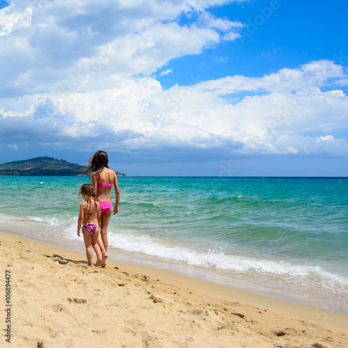 Two sisters walking on the beach in a summer day