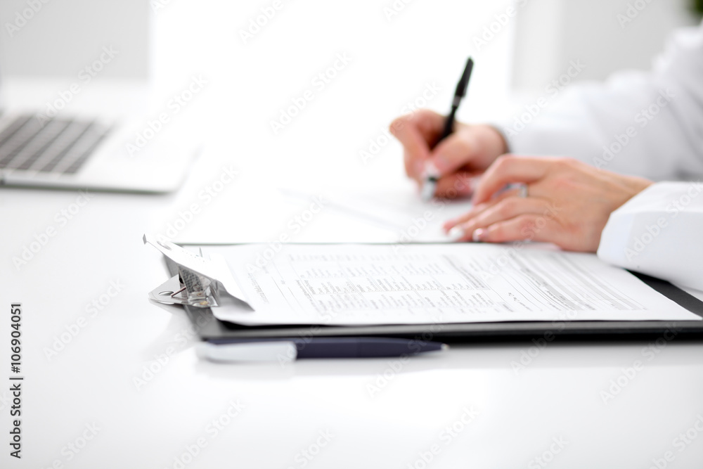 Close-up of a female doctor filling out application form , sitting at the table in the hospital Close-up of a female doctor filling out application form , sitting at the table in the hospital