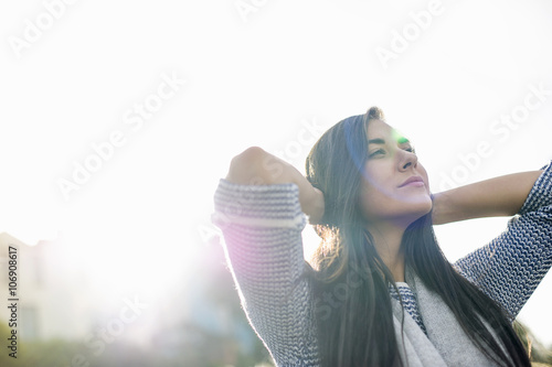 Young woman with hands behind head in sunlight