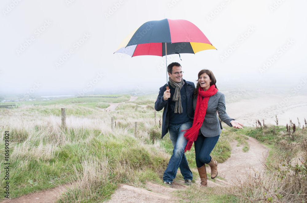 Couple on coast walk carrying umbrella, Thurlestone, Devon, UK Couple on coast walk carrying umbrella, Thurlestone, Devon, UK