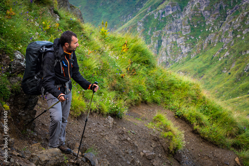 Young wet man is standing after rain at the path in the mountains of Romania, Carpathians, landscape with green grass