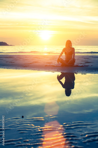 Female silhouette with reflection in water  meditation pose at sunset.