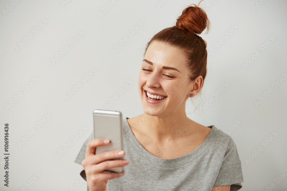 Closeup portrait smiling or laughing young freelancer woman looking at phone seeing good news or photos with nice emotion on her face isolated wall background. Human emotion, reaction, expression. Closeup portrait smiling or laughing young freelancer woman looking at phone seeing good news or photos with nice emotion on her face isolated wall background. Human emotion, reaction, expression.