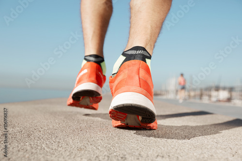 Athlete runner feet running on road closeup on shoe. Man fitness jog workout wellness concept. Man runner legs and shoes in action on road outdoors at road near sea.