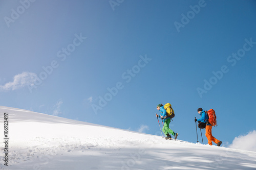 Two hikers against blue sky in winter mountains.