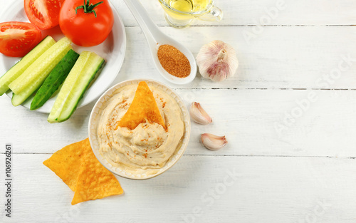 Ceramic bowl of tasty hummus with chips  oil and vegetables on table