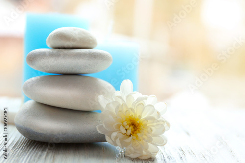Spa stones with beautiful flower and candles on white wooden table