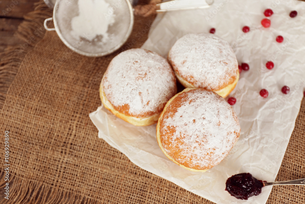 Delicious donuts with jam on parchment and sackcloth closeup