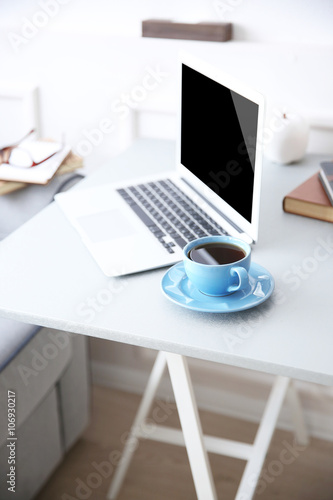 Modern interior. Comfortable workplace. Table with laptop and cup of coffee on it  close up
