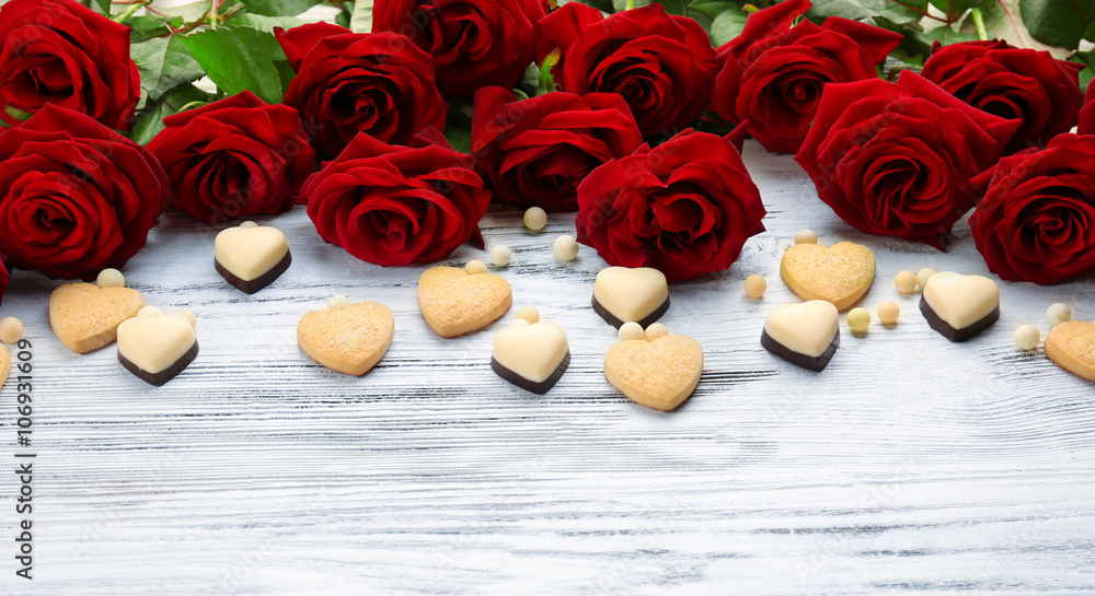 Bouquet of beautiful red roses with small cookie and candies hearts on wooden background